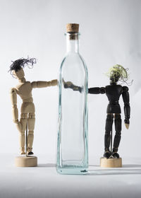 Bottle amidst wooden figurines on white background