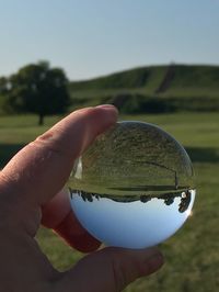 Close-up of hand holding ball against sky