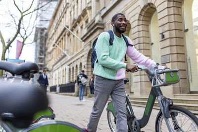 Smiling man with electric bicycle walking on footpath