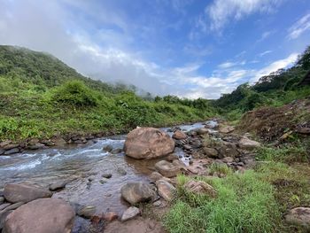 Stream flowing through rocks against sky