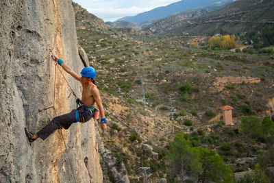 Shirtless man rock climbing against landscape