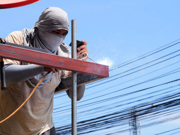 Low angle view of welder working against clear sky