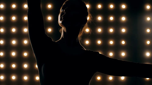 Close-up of silhouette woman dancing against illuminated lights