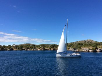 Sailboat sailing in river against blue sky