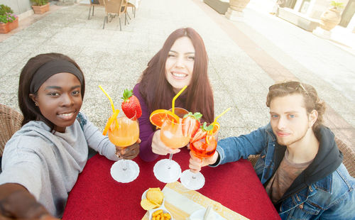 Three friends take a selfie, making cheers, celebrating multicultural friendship.