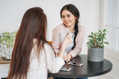 Young woman talking with friend while having coffee