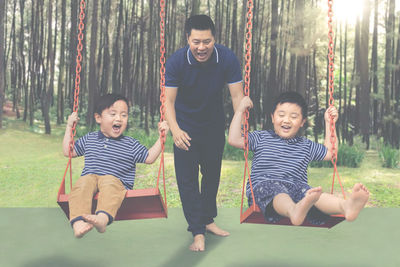 Full length of happy father swinging sons on swing in forest