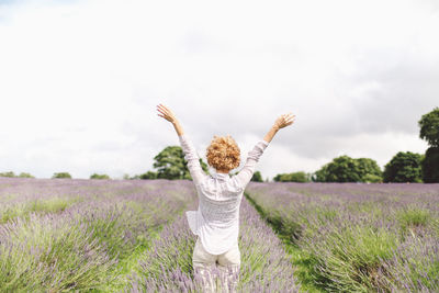Rear view of woman with arms outstretched on lavender field against sky