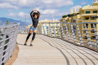 Portrait of mid adult woman with arms raised roller skating on bridge