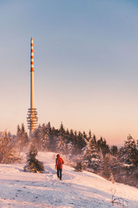 Rear view of woman standing on snow covered landscape against sky during sunset