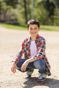 Portrait of teenager boy crouching at park