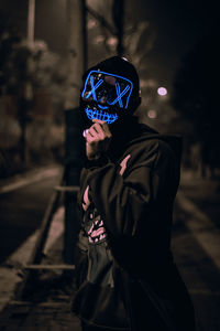 Portrait of the unknown man behind the neon mask on street at night. dark brown tone