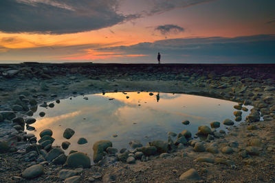 Puddle on beach against cloudy sky at sunset