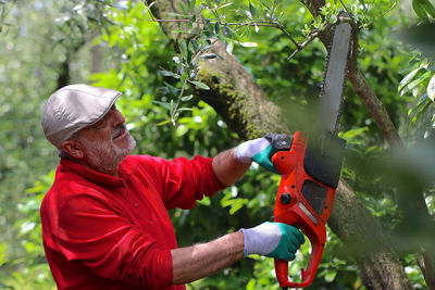 Side view of man holding plant against trees