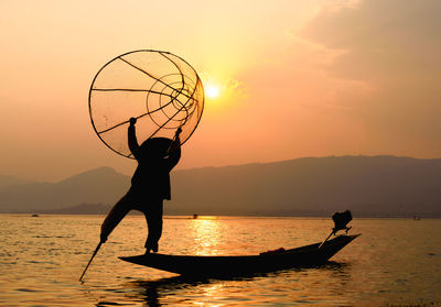 Silhouette man fishing in lake against sky during sunset