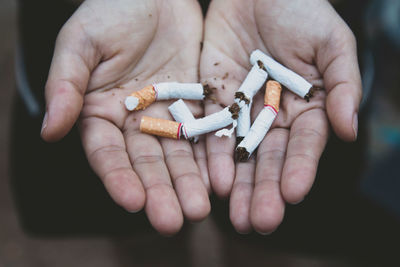 Cropped hands of person holding broken cigarettes