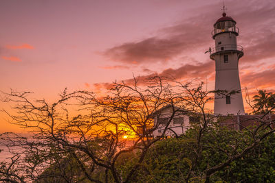 Low angle view of lighthouse by building against sky during sunset