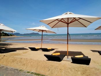 Lounge chairs and parasols on beach against sky