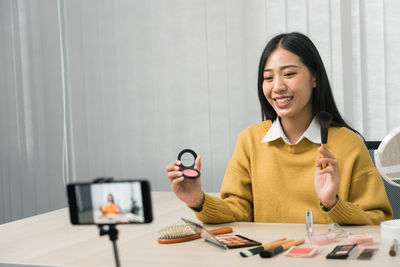 Portrait of smiling young woman using phone while sitting on table