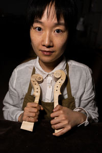 Young chinese woman violin maker showing the neck of the violins under construction in her workshop