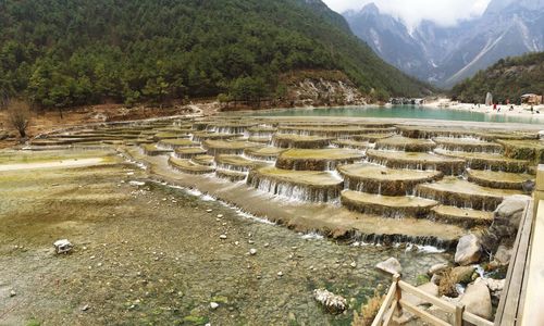 Scenic view of water flowing through rocks against mountains