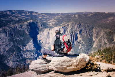 Young woman sitting on cliff against mountains