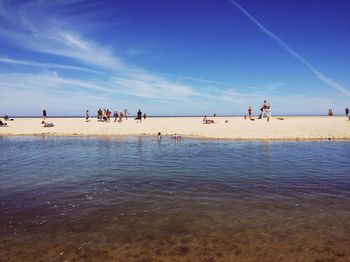 People enjoying on beach against blue sky