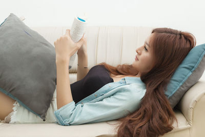 Beautiful young woman reading book on sofa at home