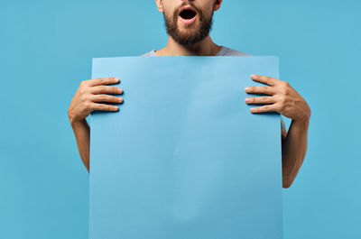 Midsection of man holding blue paper against wall