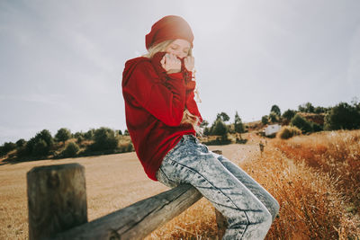 Side view of woman sitting on railing against clear sky during sunny day