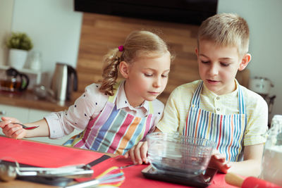 Cute sibling preparing food while reading recipe in book