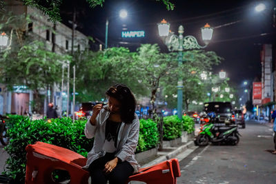 Side view of woman sitting on street in city at night