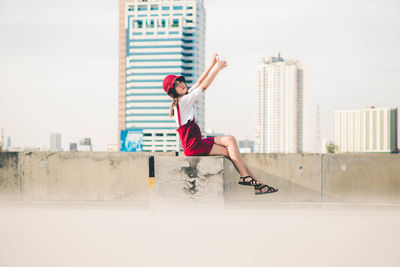 Side view of young woman jumping against buildings
