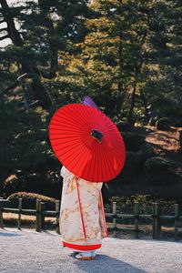 Woman with red umbrella standing on road against trees