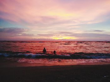 Silhouette people swimming in sea against sky during sunset