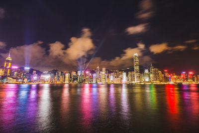 Illuminated city by river against sky at night