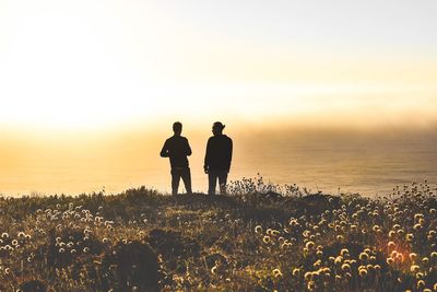 Silhouette men on beach against sky during sunset