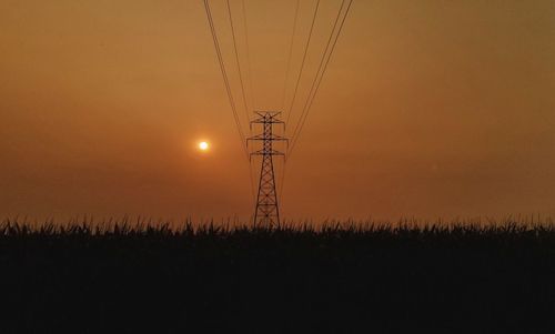 Silhouette electricity pylon on field against sky during sunset