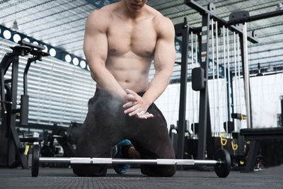 Low section of shirtless man exercising at gym