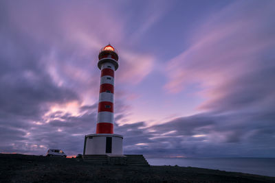 Lighthouse by sea against sky at sunset