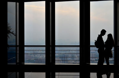 Silhouette people standing by railing against sky seen through window