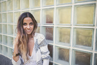 Portrait of smiling woman standing by glass window