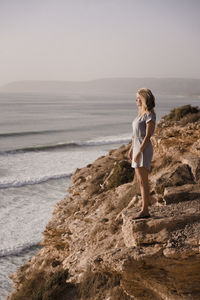 Woman standing on rock at beach against sky