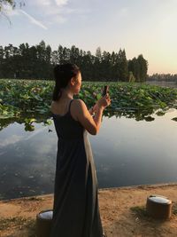 Side view of woman photographing with smart phone by lake at sunset