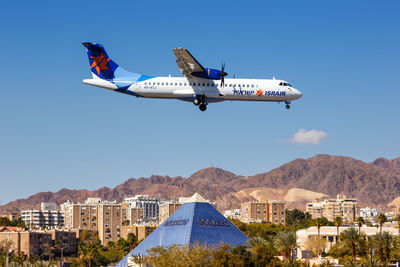 Airplane flying over buildings in city against clear blue sky