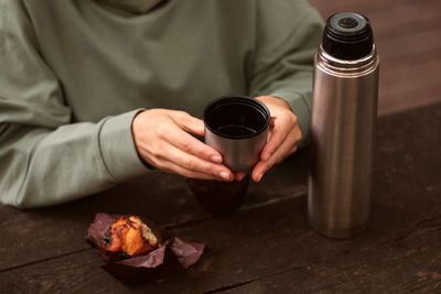 Female hands with a thermos and muffin on a wooden background outdoors