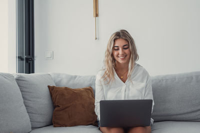 Young woman using laptop while sitting on sofa at home