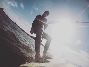 Full length of man kiteboarding against bright sky