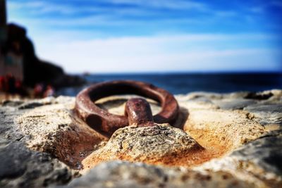 Close-up of rusty metal on rock at beach against sky