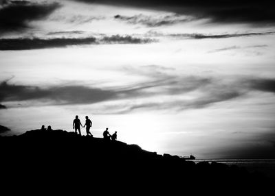 Silhouette people standing on cliff against cloudy sky